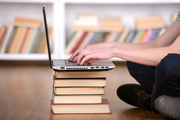 student working on a laptop on top of several books