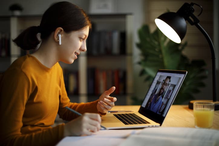 Smiling teenage girl with bluetooth headphones having video call on laptop computer at home