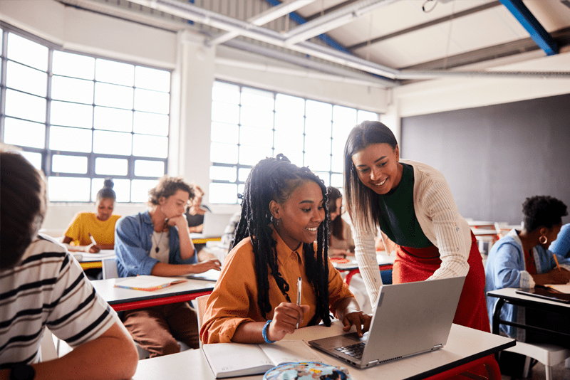 Teacher helping student in classroom in front of a PC