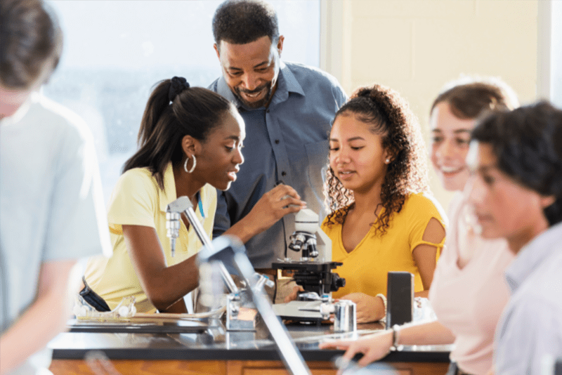 Two African American students and a teacher looking at a microscope