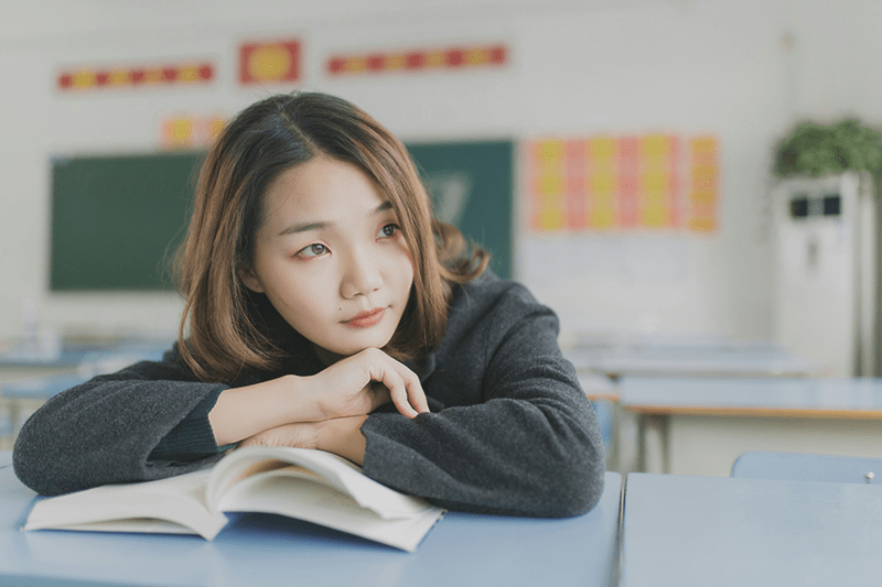 Asian student leaning on a book looking sad