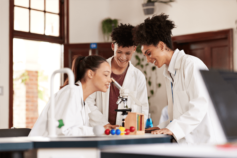 Three students standing around a microscope