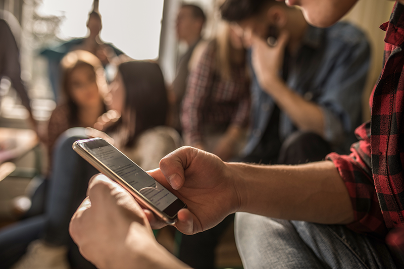 Student hand holding a smartphone with other students in the background