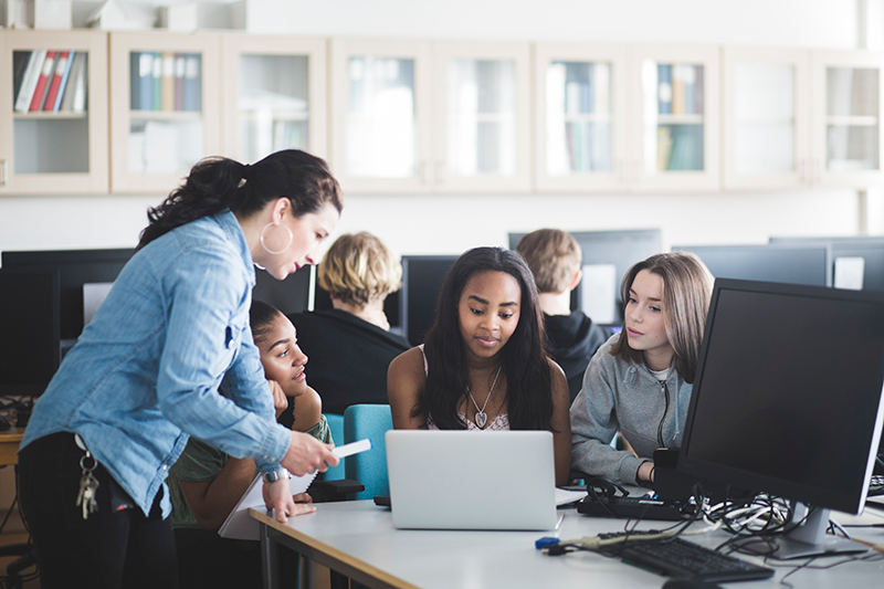 Students and teacher looking at laptop