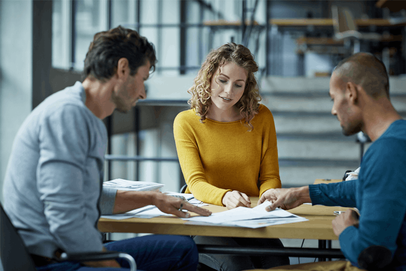 Three adults sitting at a table looking at some papers