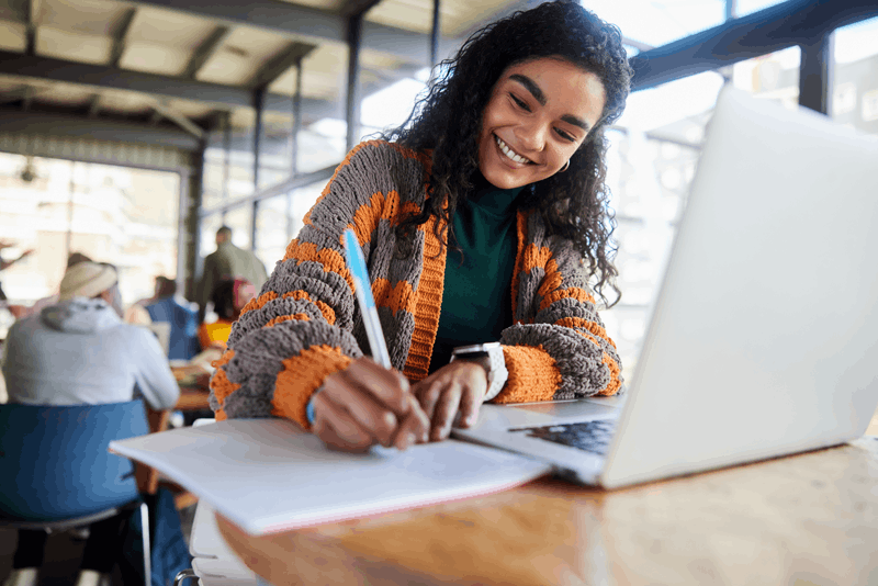 Student smiling taking notes in front of a laptop